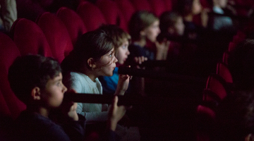 Aklais kino — skatītāji sēž kinoteātra tumsā aizsietām acīm. Katram aiz muguras atrodas bērns, kurš čukstus stāsta, kas notiek uz ekrāna.