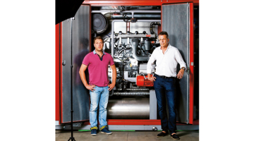 UPB koncerna vadītājs Uldis Pīlēns (pa labi) un UPB Energy valdes loceklis Māris Dzirnieks stāv pie tipiska savas ražotnes produkta — šī koģenerācijas iekārta tiks vesta uz Vāciju.