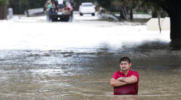 Vīrietis stāv uz applūduša ceļa pie tilta Hjūstonā. Foto: AP/LETA