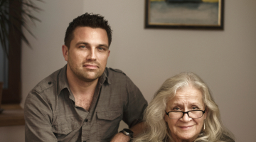 Lelde Kalmīte un Kārlis Kanderovskis Cēsu dzīvoklī. Fonā viena no Jāņa Kalmītes slavenajām rijām, kuru skaits mērāms simtos, bet varbūt pat tūkstošos.
Foto — Reinis Hofmanis