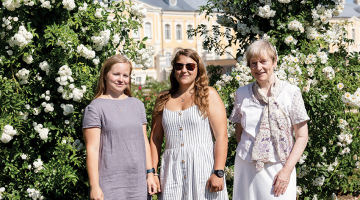 Lauma Lancmane (pa labi) ar jaunajām dārzniecēm — Leldi Ozolu un Ievu Reinvaldi — pie daiļās vīteņrozes. Foto — Ieva Salmane