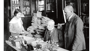 Jānis Misiņš (vidū) ar audžumeitu Hermīni un bibliofilu Fišeru savā mājas bibliotēkā Rīgā. 20. gadsimta 20. gadi. Fotogrāfs nezināms. LU bibliotēkas Misiņa bibliotēkas krājums