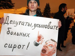 Krievijas protestētājs tur rokās plakātu ar uzrakstu: "Deputāti, adoptējiet slimos bāreņus!" Foto: EPA/LETA