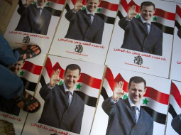 Kāds vīrs stāv uz plakātiem ar Sīrijas prezidenta Bašara al Asada portretu. Foto: AFP/LETA