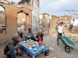 Uzbeku ģimene pie savas nopostītās mājas Ošā. Foto — AFP/LETA