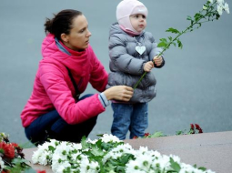 Sieviete ar bērnu noliek ziedus lielveikala jumta sabrukšanas upuriem. Foto: Evija Trifanova, LETA