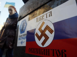 Kijevas Neatkarības laukumā pielīmēts plakāts, kas attēlo Krievijas karoga krāsas, uz kurām ir nacistu svastika. Uzraksts vēsta: okupantu krāsas. Foto: AFP/LETA
