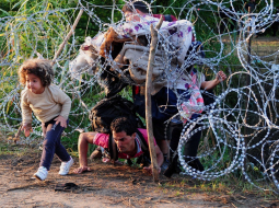 Nelegālie imigranti pie Roszke ciema uz Ungārijas-Serbijas robežas pa caurumu dzeloņdrāšu žogā šķērso robežu. Foto: AFP/LETA