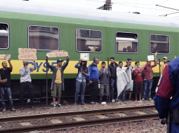 Migranti Ungārijā pie vilciena, no kura atteicās izkāpt un doties uz patvēruma meklētāju centru. Migranti improvizētos plakātos tur uzrakstus, ka vēlas doties uz Vāciju, nevis palikt Ungārijā. Foto: EPA/LETA