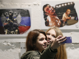 Propaganda darbībā - pērnruden izstādē Maskavā meitenes fotografējas - fonā Putina "spēku" slavinoši "mākslas darbi": Putins boksā uzvar ukraini Vitāliju Kļičko. Foto: EPA/LETA