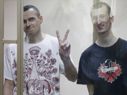 Oļegs Sencovs (no kreisās) Rostovas tiesas zālē rāda uzvaras zīmi sprieduma nolasīšanas laikā. Viņam līdzās - Aleksandrs Koļčenko, kuram tiesa piesprieda 10 gadus cietumā. Foto: ITAR-TASS/LETA