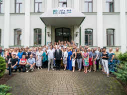 Izdevniecības darbinieki pie ēkas ar jauno logo. Publicitātes foto