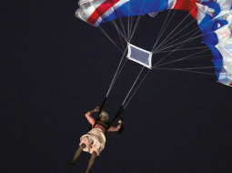 Aktieris imitē britu karalienes Elizabetes II nolaišanos no helikoptera olimpiskajā stadionā.