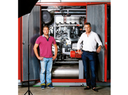 UPB koncerna vadītājs Uldis Pīlēns (pa labi) un UPB Energy valdes loceklis Māris Dzirnieks stāv pie tipiska savas ražotnes produkta — šī koģenerācijas iekārta tiks vesta uz Vāciju.
