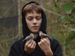 Papes ornitoloģiskajā stacijā var mācīties par putniem un redzēt, kā tos gredzeno, stāsta putnu fotogrāfs Miķelis Zalāns, kurš rokās tur parastos ķeģus. «Tos noķer tīklos un uz kājām uzliek metāla gredzentiņus. Tas nenodara putnam sāpes, bet cilvēkiem palīdz izsekot tā migrācijas ceļu.»
Foto — Matīss Fjodorovs