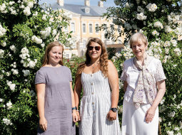 Lauma Lancmane (pa labi) ar jaunajām dārzniecēm — Leldi Ozolu un Ievu Reinvaldi — pie daiļās vīteņrozes. Foto — Ieva Salmane