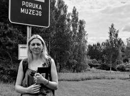 Rakstniece Inga Žolude autobusu pieturā, kas atrodas netālu no Vecās skolas, kurā mācījies Jānis Poruks. Skolā saglabāta autentiska mācību klasīte no viņa laika un rakstnieka dzīves un daiļrades izzināšanai atvēlēta  istabiņa.
Foto no Ingas Žoludes privātā arhīva