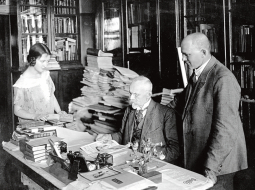 Jānis Misiņš (vidū) ar audžumeitu Hermīni un bibliofilu Fišeru savā mājas bibliotēkā Rīgā. 20. gadsimta 20. gadi. Fotogrāfs nezināms. LU bibliotēkas Misiņa bibliotēkas krājums