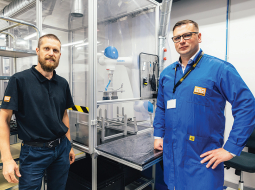 Produktivitātes rādītājus HansaMatrix Ventspils ražotnē uzlabo, izmantojot arī robotu roku darbu, rāda Edžus Siliņš (pa kreisi) un Dāvis Šnikvalds.