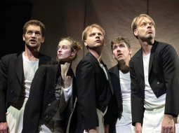 Melnās frakās tērpušies, izrādes aktieri — Edgars Ozoliņš, Polina Čerņenoka, Kārlis Ērglis, Hugo Puriņš un Gatis Maliks — sarunājas kā tās caunas, kuras seši mazi bundzenieki padarījuši par cepurēm. Foto — Aigars Hibneris